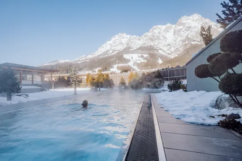 Outdoor thermal pool surrounded by snow with mountain view in alpine resort